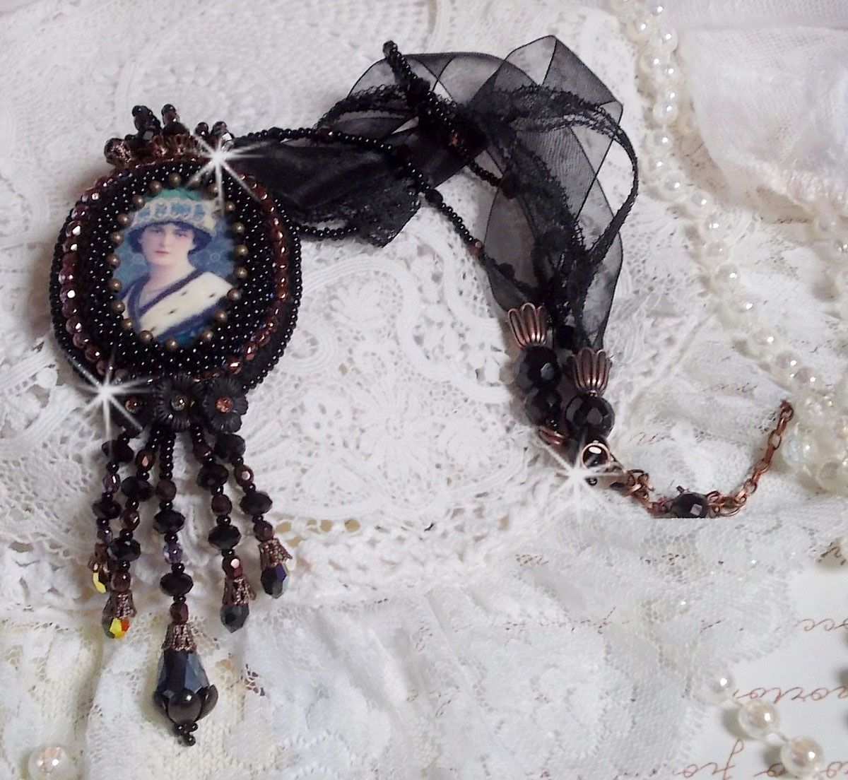 Pendentif Midnight Daisy avec un cabochon en bois repr&eacute;sentant une femme en chapeau Bleu, brod&eacute; avec des fleurs lucites, coupelles et facettes. Le tout est fini avec une dentelle Noire et un ruban