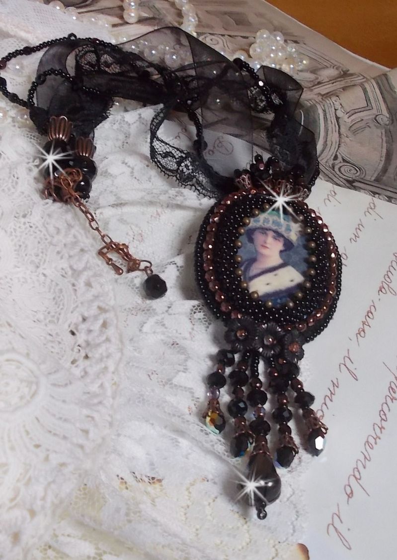 Pendentif Midnight Daisy avec un cabochon en bois repr&eacute;sentant une femme en chapeau Bleu, brod&eacute; avec des fleurs lucites, coupelles et facettes. Le tout est fini avec une dentelle Noire et un ruban