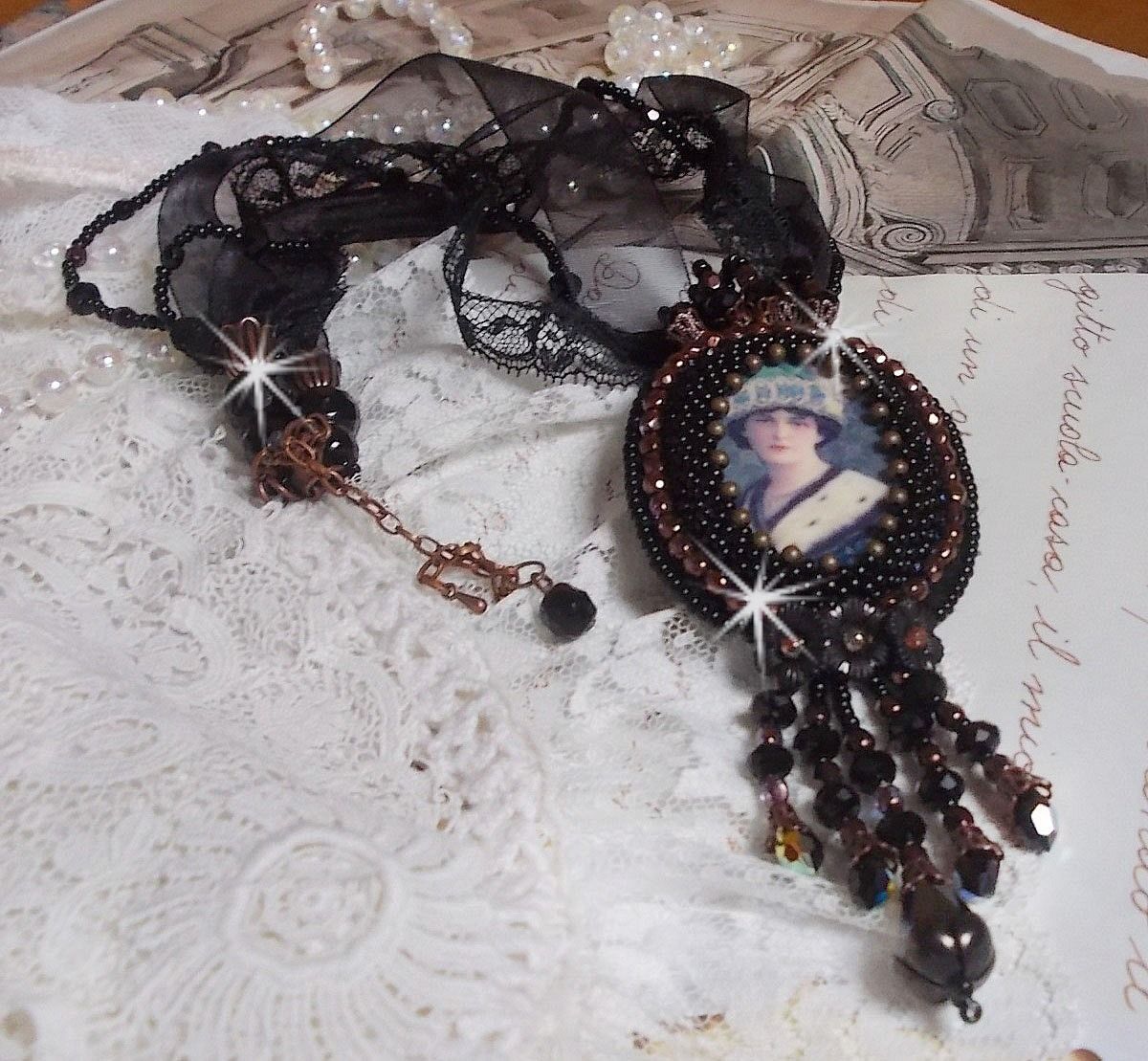 Pendentif Midnight Daisy avec un cabochon en bois repr&eacute;sentant une femme en chapeau Bleu, brod&eacute; avec des fleurs lucites, coupelles et facettes. Le tout est fini avec une dentelle Noire et un ruban