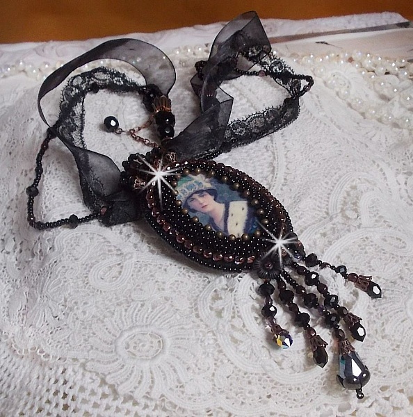 Pendentif Midnight Daisy avec un cabochon en bois repr&eacute;sentant une femme en chapeau Bleu, brod&eacute; avec des fleurs lucites, coupelles et facettes. Le tout est fini avec une dentelle Noire et un ruban