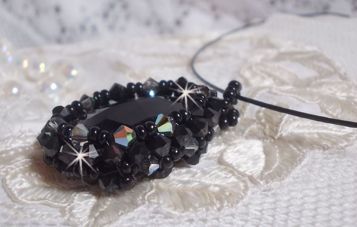 Pendentif Mirano incarne parfaitement l&rsquo;&eacute;l&eacute;gance avec un cabochon ovale facett&eacute; en Cristal cercl&eacute; de rocailles et toupies aux couleurs Noires et Argent&eacute;es. Mont&eacute; sur un tour du cou c&acirc;bl&eacute; et cir&eacute; Noir 