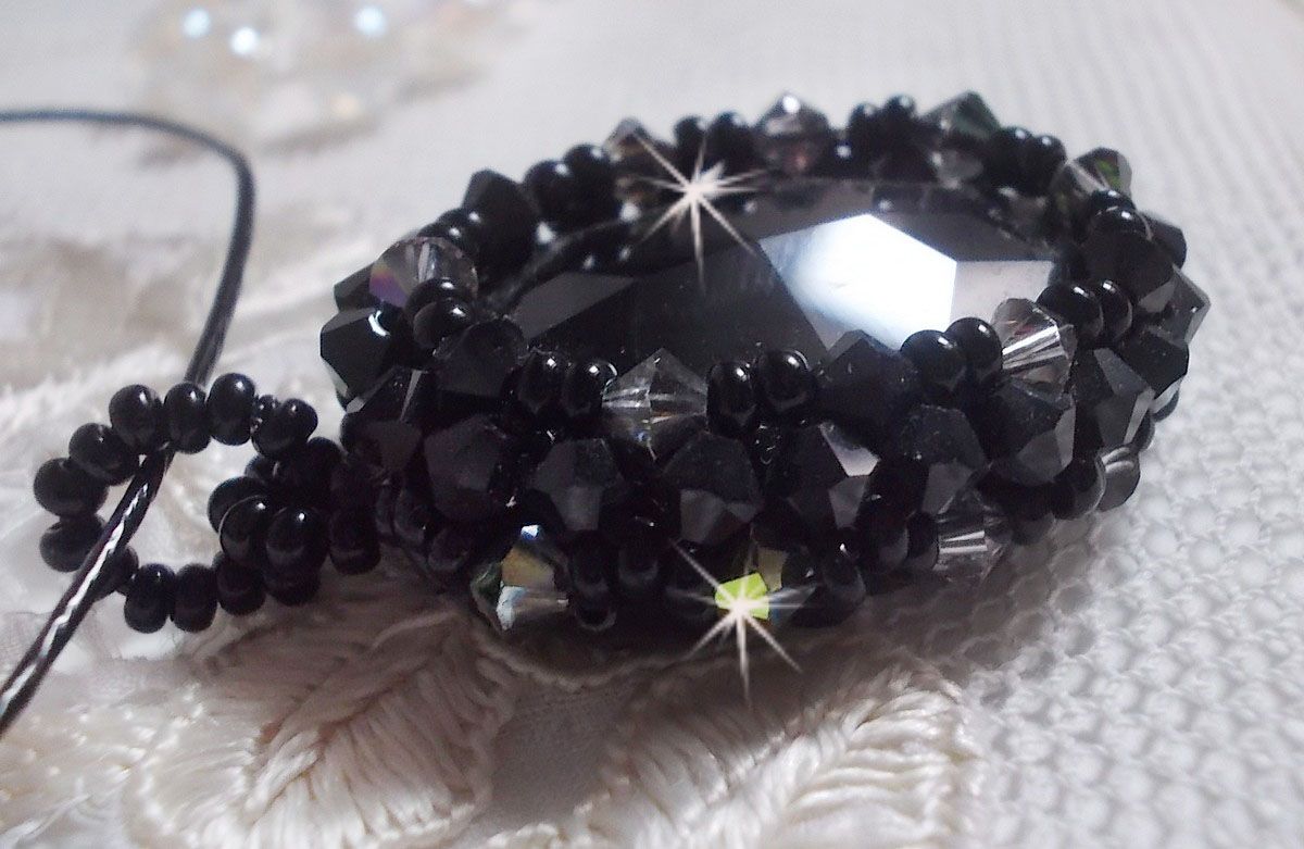 Pendentif Mirano incarne parfaitement l&rsquo;&eacute;l&eacute;gance avec un cabochon ovale facett&eacute; en Cristal cercl&eacute; de rocailles et toupies aux couleurs Noires et Argent&eacute;es. Mont&eacute; sur un tour du cou c&acirc;bl&eacute; et cir&eacute; Noir 