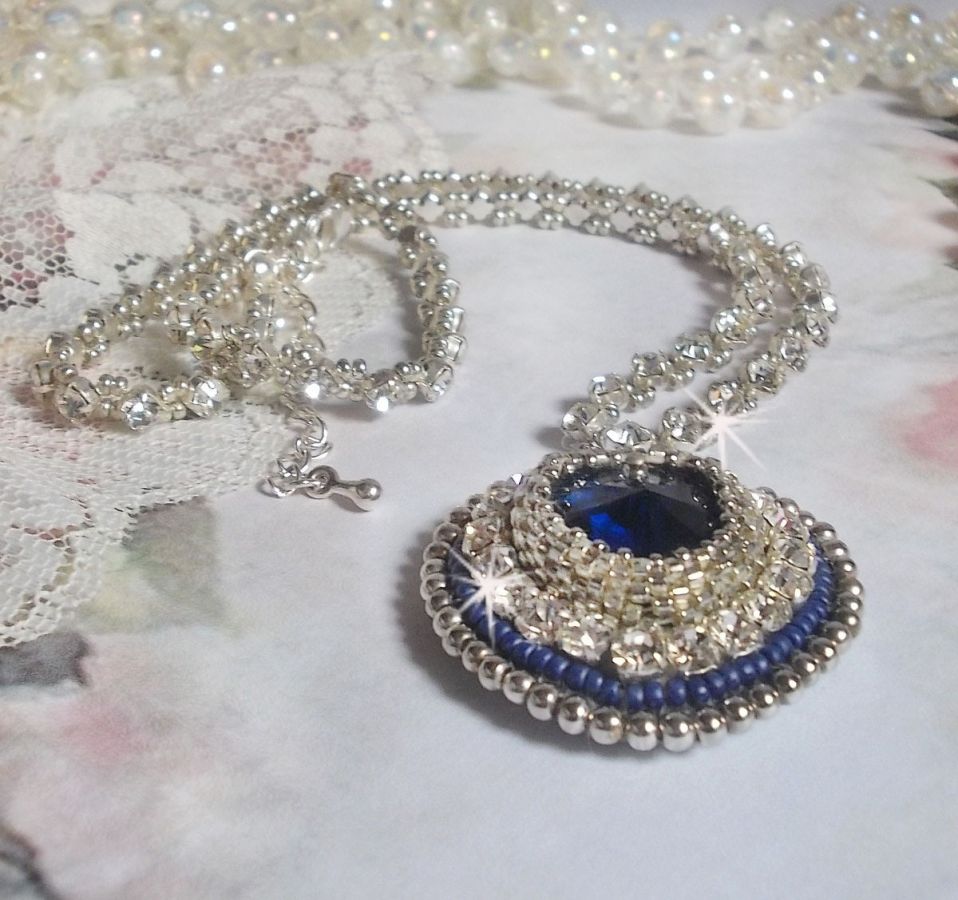 Collier Saphir Bleu brod&eacute; &agrave; l'aiguille avec un c&oelig;ur en cristal de Swarovski, rocailles argent&eacute;es Miyuki, strass, un fermoir et une cha&icirc;nette d'extension en argent 925/1000. Un voyage si lointain.