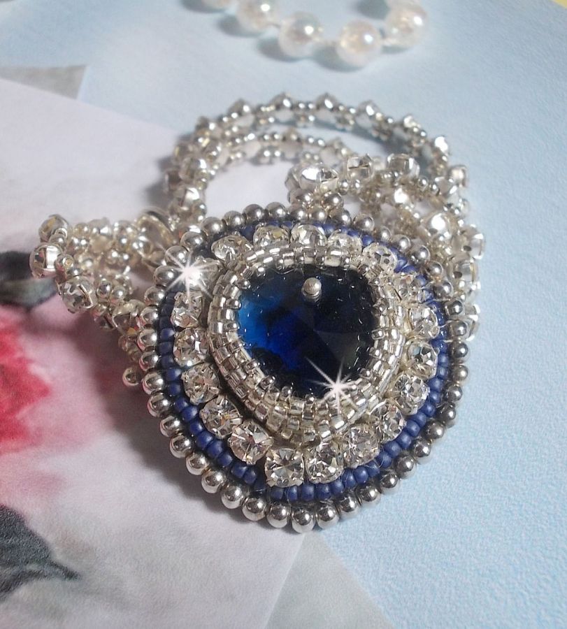 Collier Saphir Bleu brod&eacute; &agrave; l'aiguille avec un c&oelig;ur en cristal de Swarovski, rocailles argent&eacute;es Miyuki, strass, un fermoir et une cha&icirc;nette d'extension en argent 925/1000. Un voyage si lointain.