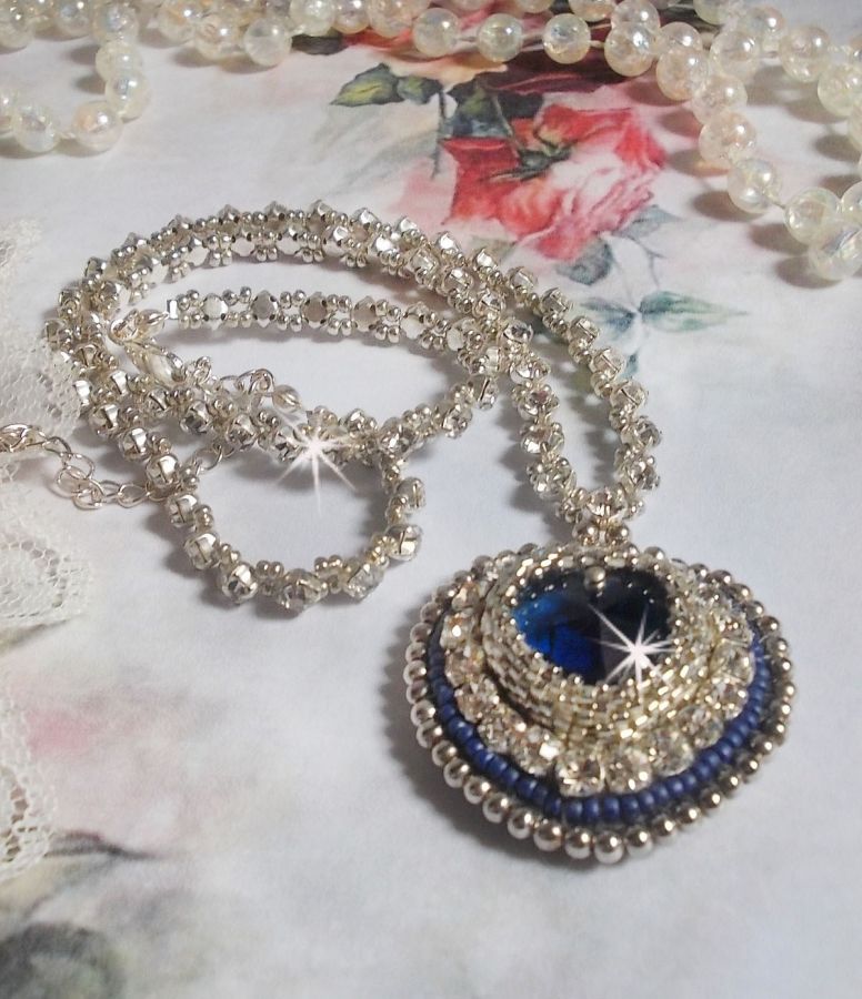 Collier Saphir Bleu brod&eacute; &agrave; l'aiguille avec un c&oelig;ur en cristal de Swarovski, rocailles argent&eacute;es Miyuki, strass, un fermoir et une cha&icirc;nette d'extension en argent 925/1000. Un voyage si lointain.