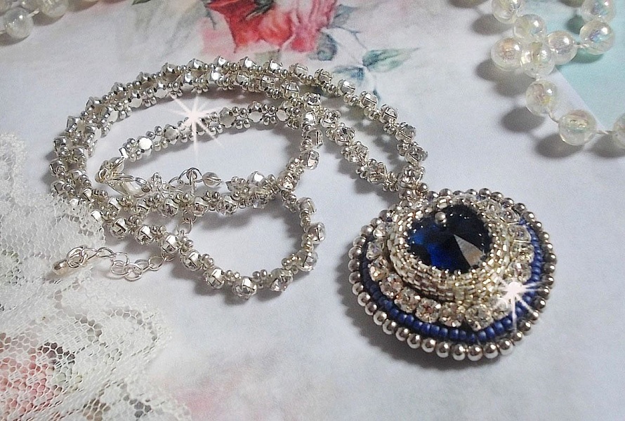 Collier Saphir Bleu brod&eacute; &agrave; l'aiguille avec un c&oelig;ur en cristal de Swarovski, rocailles argent&eacute;es Miyuki, strass, un fermoir et une cha&icirc;nette d'extension en argent 925/1000. Un voyage si lointain.