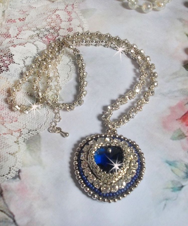 Collier Saphir Bleu brod&eacute; &agrave; l'aiguille avec un c&oelig;ur en cristal de Swarovski, rocailles argent&eacute;es Miyuki, strass, un fermoir et une cha&icirc;nette d'extension en argent 925/1000. Un voyage si lointain.