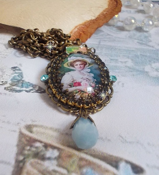 Pendentif Douce Dame cr&eacute;&eacute; avec un cabochon repr&eacute;sentant une femme au chapeau blanc orn&eacute; de cristaux, des accessoires de couleur Bronze et un jade teint&eacute; bleu 