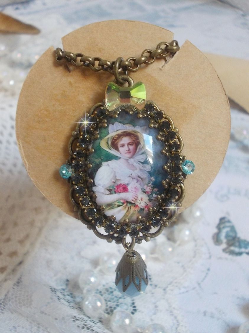 Pendentif Douce Dame cr&eacute;&eacute; avec un cabochon repr&eacute;sentant une femme au chapeau blanc orn&eacute; de cristaux, des accessoires de couleur Bronze et un jade teint&eacute; bleu 