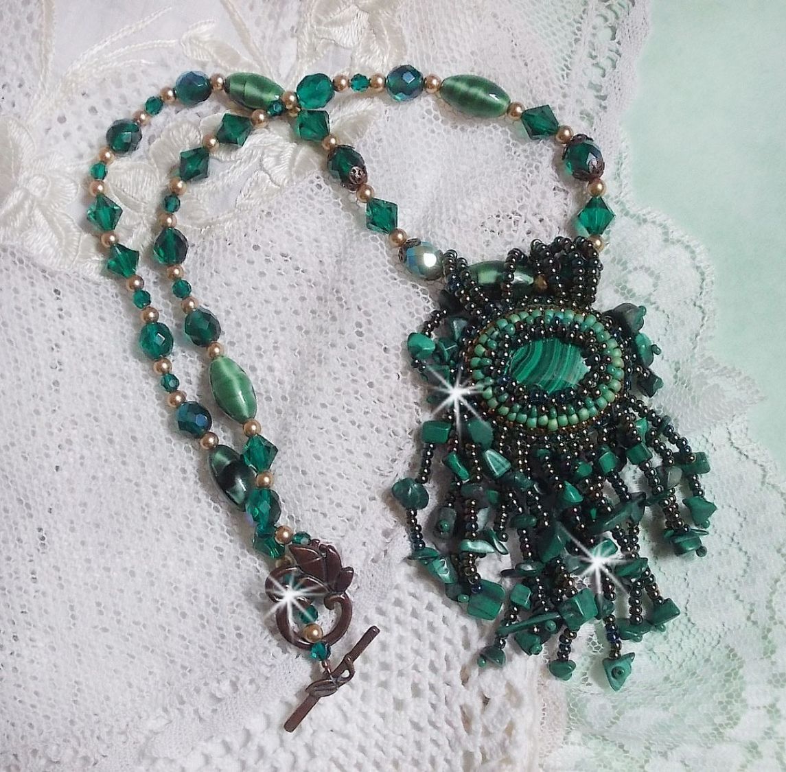 Pendentif Emerald avec un cabochon ovale en Malachite orn&eacute; de chips avec cristaux : perles rondes et toupies Emerald. S&rsquo;ajoute des perles en forme d&rsquo;olives. Brod&eacute;s sur fermoir en T. Un style Ethnique