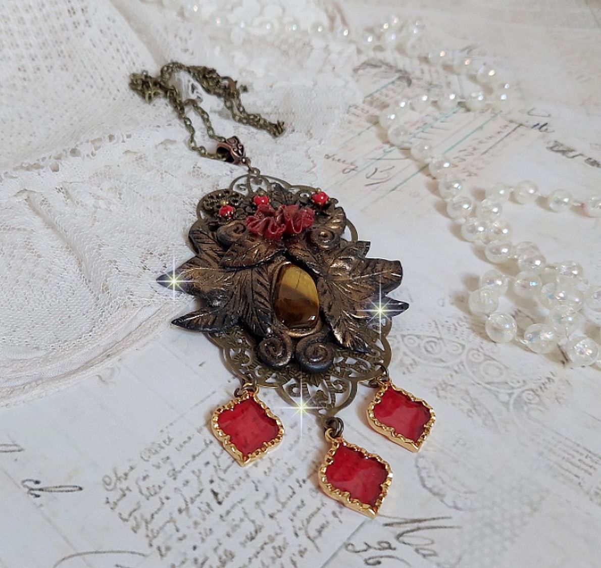 Pendentif M&eacute;lodie avec un cabochon &OElig;il de tigre orn&eacute; de perles en Jade Rouge vein&eacute; de Noir sur fleurs 5 p&eacute;tales et estampes mont&eacute;s sur une cha&icirc;ne bronze. Les pendants sont en r&eacute;sine &eacute;poxy Rouge