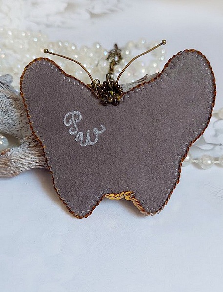 Dos du pendentif papillon brodé avec signature artisanale.