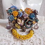 Broche Eclats P&eacute;tillants d&rsquo;inspiration Baroque, orn&eacute;e de fleurs en r&eacute;sine autour d&rsquo;un cabochon strass&eacute;s et perl&eacute;s sur estampes, cristaux, breloques, perle cloisonn&eacute;e, perles jaunes en verre et roses. 