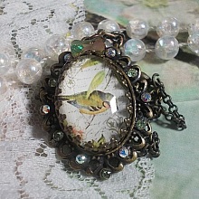 Collier Oiseau des Jardins s&rsquo;inspire d&rsquo;un oiseau dans la nature. Sur une base d&rsquo;un pendentif, ce motif est orn&eacute; de cristaux : n&oelig;ud et cabochons aux nuances cristal et P&eacute;ridot. Mont&eacute; sur cha&icirc;ne Laiton