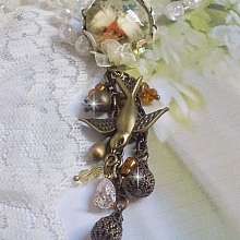 Broche Colombes aux plumages blancs avec des breloques filigran&eacute;es gouttes et lisses, perles rondes et n&oelig;ud en cristal, ruban organza cr&egrave;me, pendentif plaqu&eacute; or avec un zircon sur une broche en m&eacute;tal