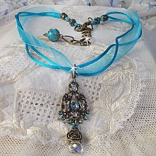 Pendentif Lady in Blue mont&eacute; avec des chandeliers, des cristaux : cabochons, perles rondes et toupies, perles en c&eacute;ramique, cabochons Zirconium, rocailles et rubans. Tout est de couleur Bleu et Bronze
